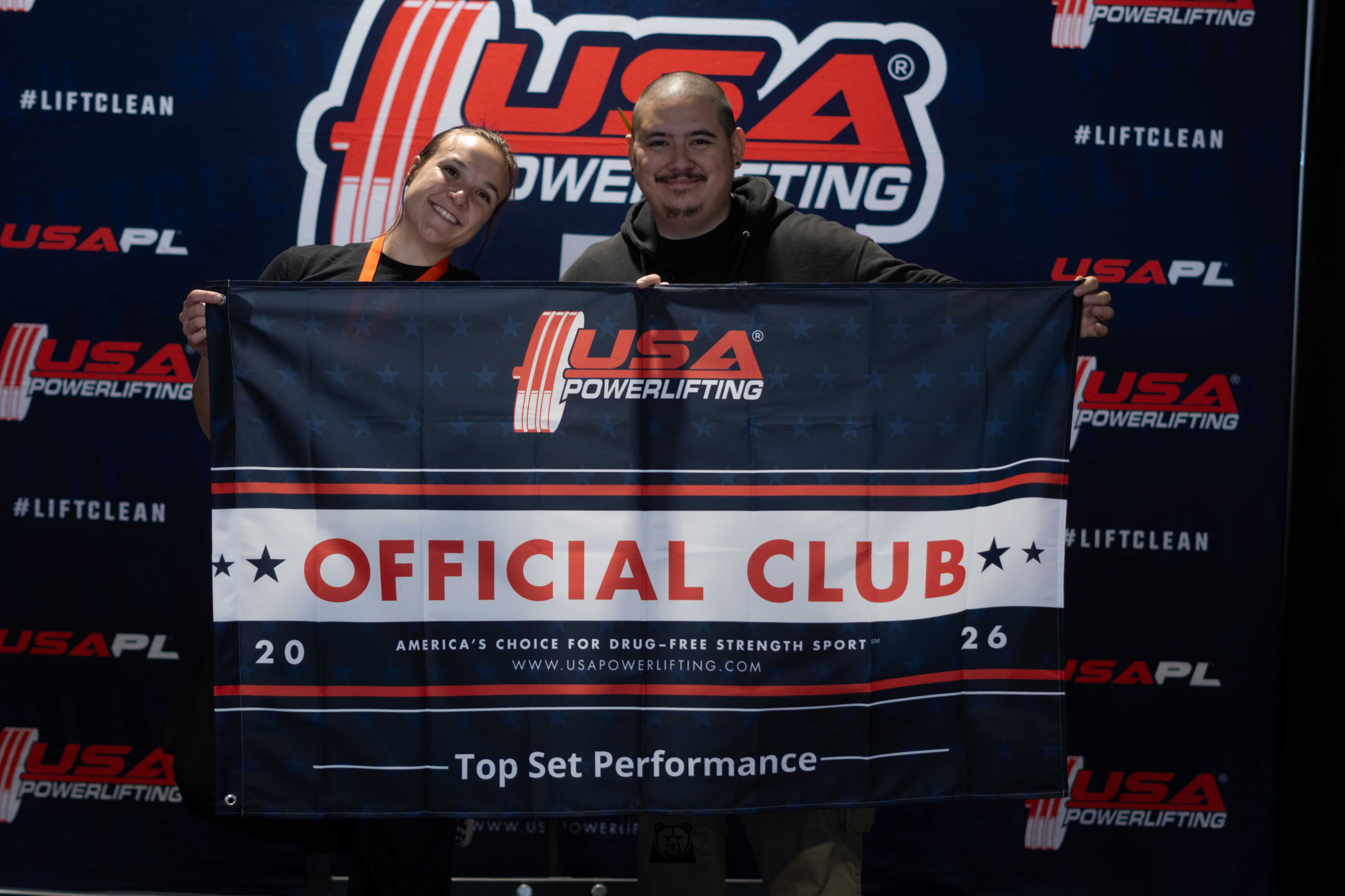 Coach Trujillo and an Iron Mavericks athlete holding a USA Powerlifting Official Club banner