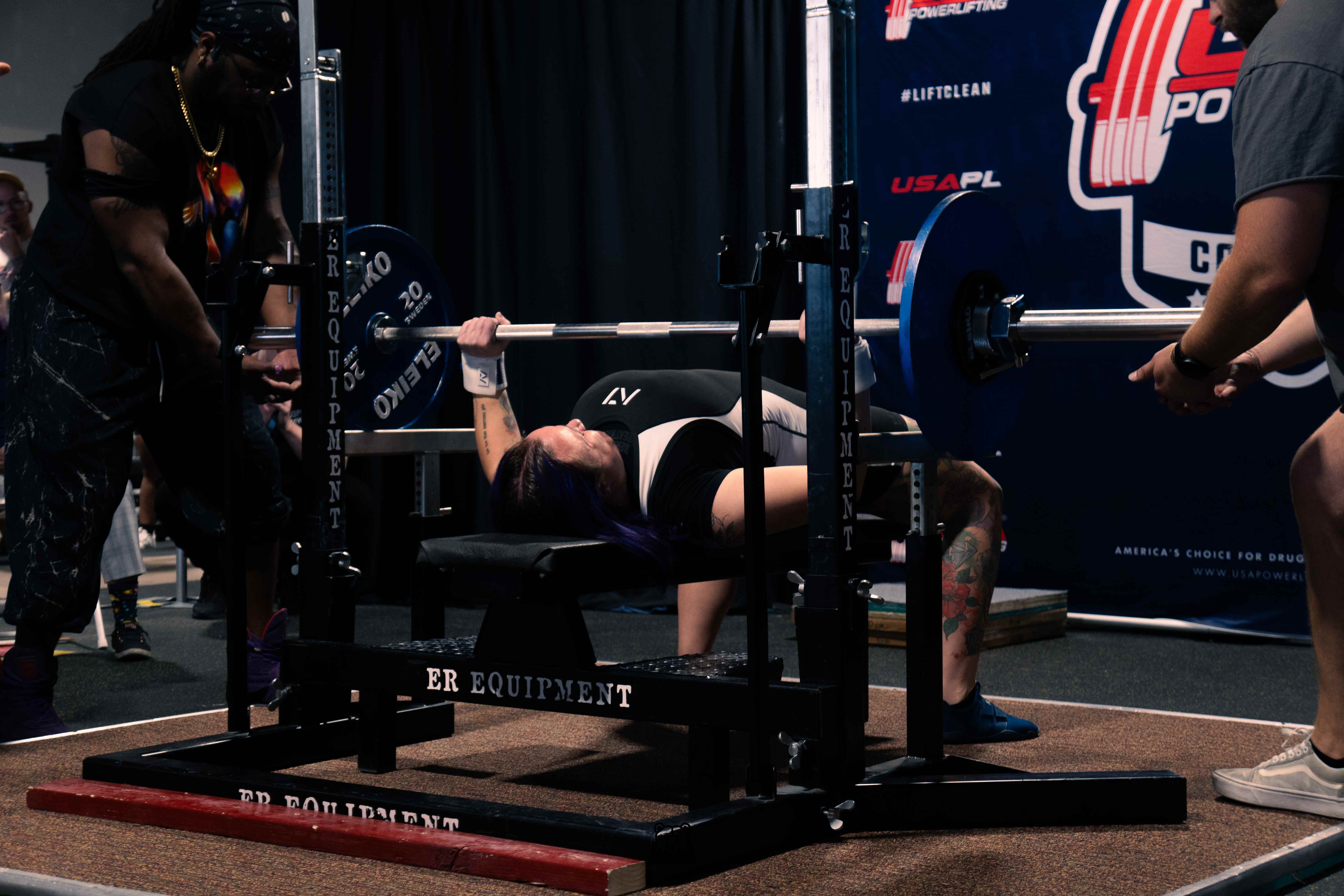 Powerlifter bench pressing with spotters at a USA Powerlifting meet
